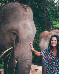 Portrait of woman touching elephant while standing in zoo