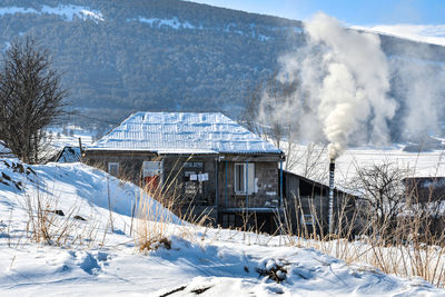 Smoke emitting from snow covered building against mountain