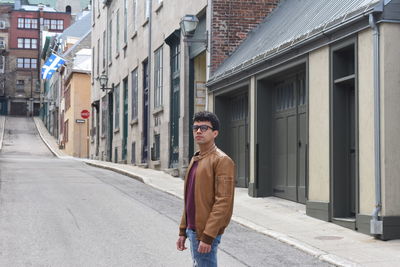 Portrait of young man standing on street against buildings