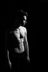 Shirtless handsome young man standing against black background