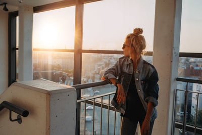 Woman standing by railing against window