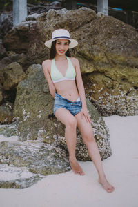 Full length of smiling woman sitting on rock at beach