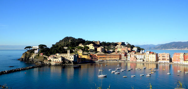 Buildings by sea against clear blue sky