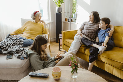 Mother and son talking with senior woman sitting on chair at home