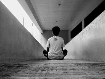 Rear view of boy sitting on wall in building