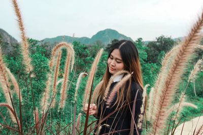 Beautiful young woman with plants in background against sky