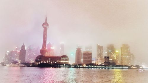 Illuminated buildings by river against sky in city