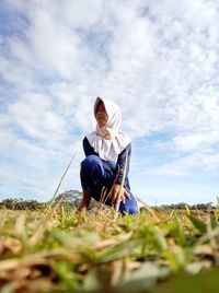 Low angle view of woman sitting on field against sky