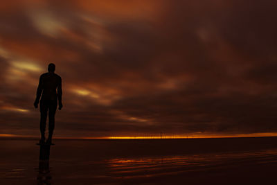 Silhouette man standing by sea against sky during sunset