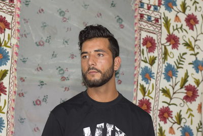 Portrait of young man standing against curtain