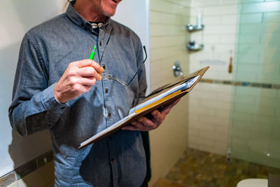 Midsection of man holding clipboard at bathroom