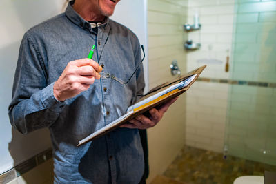 Midsection of man holding paper while standing against wall