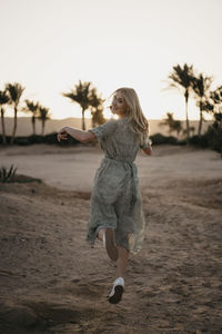 Woman standing on beach against sky during sunset