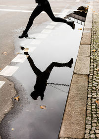 Low section of man jumping over puddle on street during rainy season