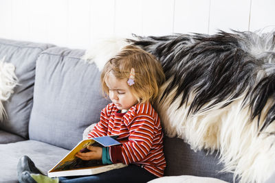 Girl reading book while sitting on sofa at home