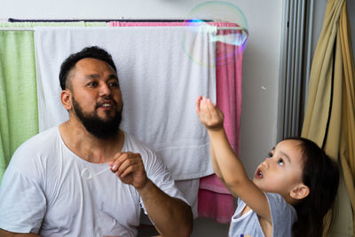Father blowing bubbles with daughter at home