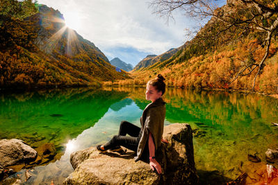 Woman sitting on rock by lake against mountains