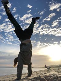 Rear view of people at beach against sky during sunset