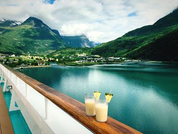 Drinks on railing of boat at lake against mountains 