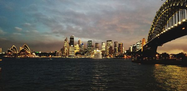 Illuminated city by sea against sky