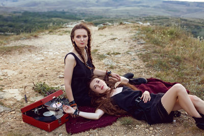 Two hippie woman are lying in a field on a mountain with an old gramophone on a vinyl record