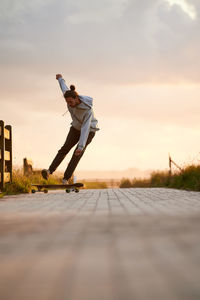 Ground level of full body of male in casual wear performing stunt on longboard on paved walkway