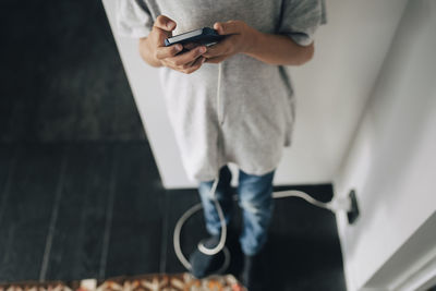 Low section of boy using smart phone while standing in room at home
