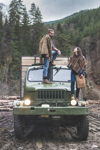 Young woman looking at man standing on truck in forest