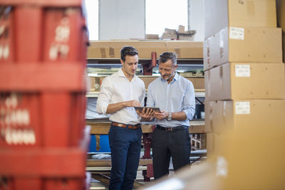 Two businessmen in factory storeroom looking at tablet