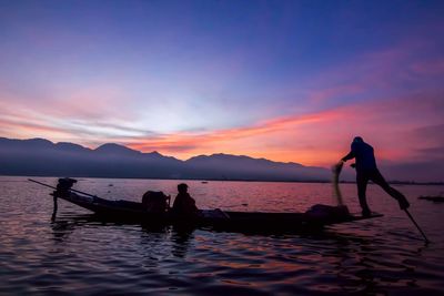 Man fishing on lake against sky during sunset