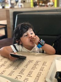 Cute boy with phone sitting in restaurant