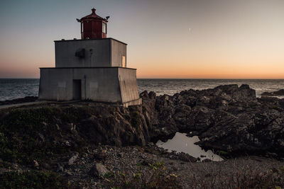 Lighthouse by sea against sky during sunset