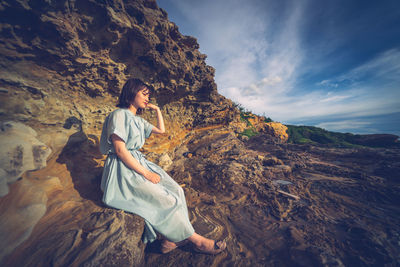 Full length of young woman sitting on rock