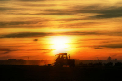 Silhouette tractor on field against sky during sunset