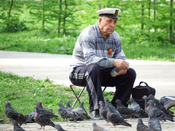 Senior man sitting on foldable chair while feeding pigeons at park