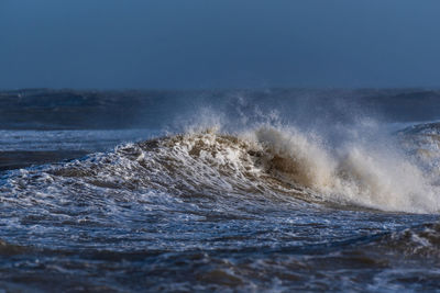 Waves splashing in sea against clear sky