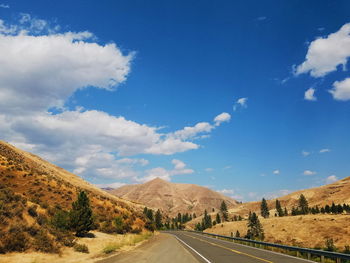 Road leading towards mountains against blue sky