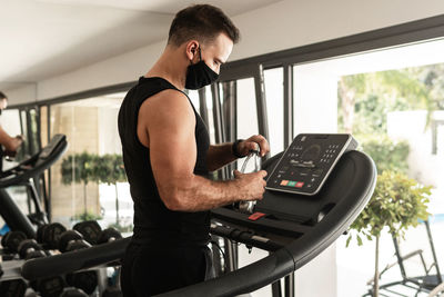 Man wearing mask holding water bottle while standing on treadmill