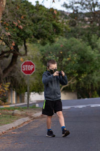 Cute boy photographing while standing by road