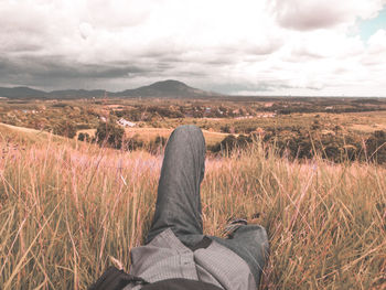 Low section of man relaxing on field against sky