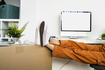 Tired young woman leaning legs on cardboard box while moving into new apartment