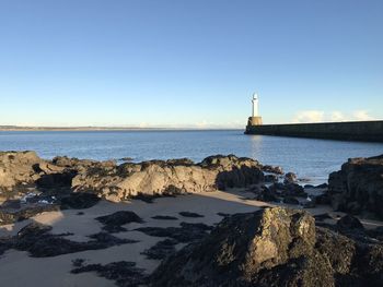 Lighthouse by sea against clear blue sky