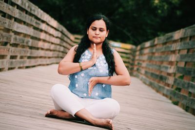 Full length of woman meditating while sitting on walkway