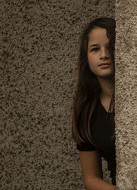 Portrait of girl hiding behind wall