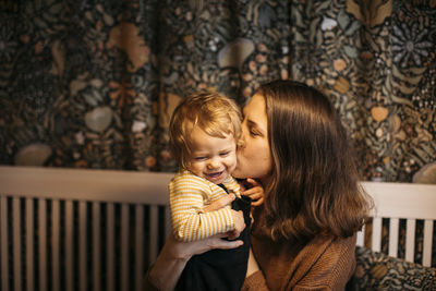 Mother kissing son on cheek at home