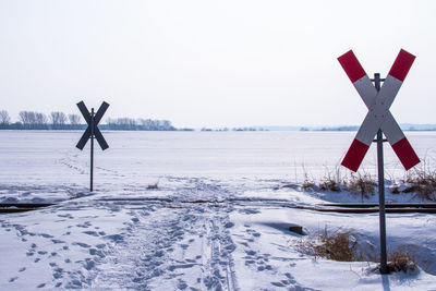 Road sign on snow covered field against clear sky