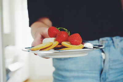 Midsection of woman holding biscuits with strawberries and cheese in plate