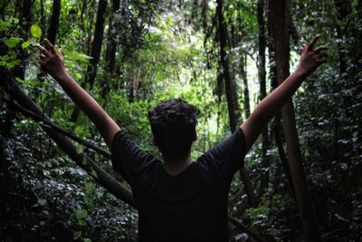 Rear view of teenage boy with arms outstretched standing in forest