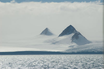 Scenic view of sea and snowcapped mountains against sky