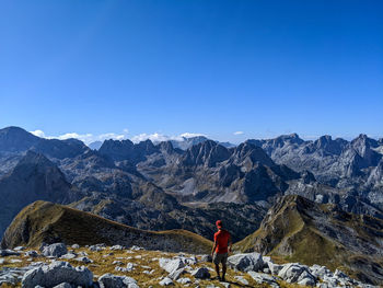 Rear view of person standing on snowcapped mountain against blue sky